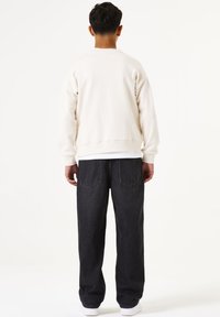 Crème sweatshirt met lange mouwen en geribde manchetten, gecombineerd met donkere spijkerbroek. De outfit heeft een relaxte pasvorm en minimale details.