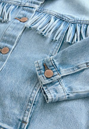 Lichtblauwe denimjack met franjes op de schouders, metalen drukknoopjes en contraststiksels. Zachte textuur en casual ontwerp.