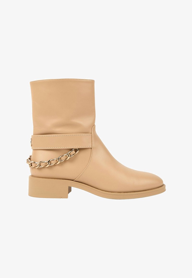 Botte en cuir beige mi-mollet avec un talon bloc bas et un détail décoratif avec une chaîne dorée enroulée autour de la sangle arrière.