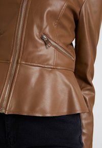 Giacca in ecopelle marrone con orlo peplum, chiusura con zip frontale e tasca con zip laterale. Texture liscia e design aderente.
