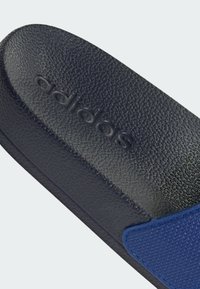 Chancla Adidas con una plantilla texturizada negra y una correa azul con detalles de costura. El diseño es minimalista y práctico.