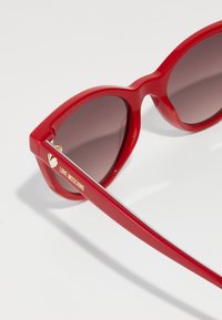 Red plastic cat-eye sunglasses with gradient brown lenses. Features gold "LOVE MOSCHINO" branding on the arm and a heart accent.