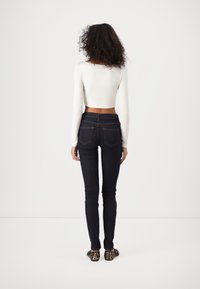 Jeans ajustados de mezclilla oscura con costuras naranjas y bolsillos traseros, acompañados de una blusa ajustada de manga larga color crema y zapatos de estampado de leopardo.