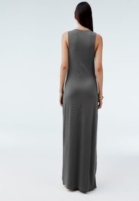 Długa sukienka maxi bez rękawów w ciemnoszarym kolorze, o dopasowanym kroju, miękkiej fakturze i prostym wykończeniu, sięgająca do kostek.