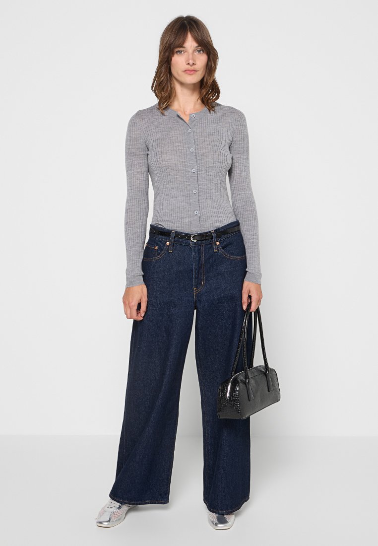 Graues, geripptes Langarm-Hemd mit Knopfleiste und Rundhalsausschnitt, kombiniert mit weit geschnittenen, dunkelblauen Jeans und einer schwarzen Handtasche.