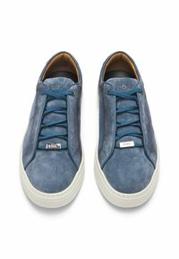 Blå mockaskor med texturerat ovandel, tonade snörning och vit gummisula. Har en metallisk logotypdetalj på sidan.