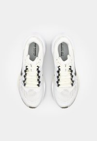 Bijele atletske cipele s mrežastim gornjim dijelom, crnim kontrastnim swoosh-om, bež naglascima i teksturiranim potplatom. veze su reflektirajuće.