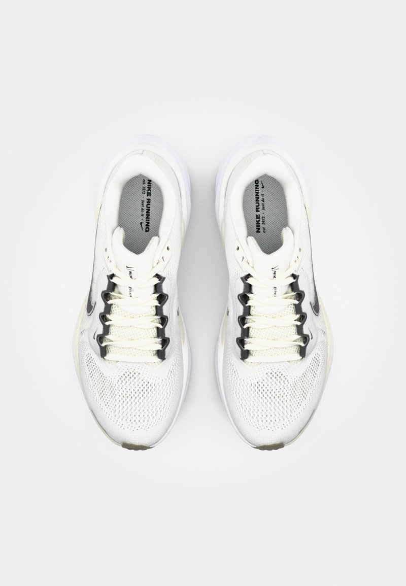 Zapatillas deportivas blancas con parte superior de malla, distintivo swoosh negro, acentos beige y suela texturizada. Los cordones son reflectantes a la luz.