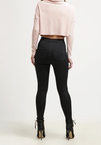 Schwarze Skinny-Jeans mit Gesäßtaschen, kombiniert mit einem kurz geschnittenen hellrosa Sweatshirt. Die Model trägt hochhackige schwarze Schnürstiefel.