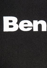 Czarna tkanina z wyraźnym białym logo "Ben" w pogrubionej czcionce. Tekstura wydaje się być tkana, co nadaje jej trwałe wykończenie.