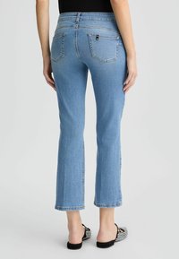 Jean évasé bleu clair avec taille mi-haute, cinq poches, couture apparente et détail de bord brut à l'ouverture des jambes.