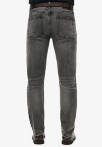 Jeans de denim gris con corte recto, cinco bolsillos y un desgaste sutil. Incluye un cinturón de cuero marrón con una hebilla de plata.