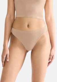 Beige cotton blend thong with a smooth texture, minimal elastic waistband, and seamless design, providing a discreet fit under clothing.