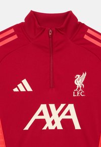 Punane sportlik pullover kõrge kraega, pooleldi lukuga, valge Liverpool FC logoga, "AXA" logoga ja kolme valge Adidas triibuga õlgadel.