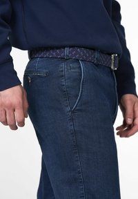 Jeans en denim bleu foncé avec un léger délavage et deux poches avant, complétés par une ceinture tissée bleue marine avec des accents bleu clair et une boucle en argent.