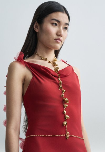 Vörös selyemruha drapált dekoltázzsal, áttetsző rózsaszín tüll dekorációval a vállakon és arany medál lánc részlettel.