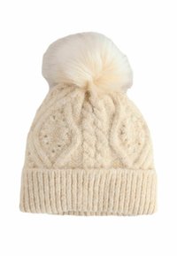 Knit cream beanie with cable pattern, ribbed cuff, and a fluffy pom-pom on top. Made of soft material, textured finish.