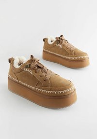 Sneaker platform in suede marrone con fodera soffice, cuciture decorative e lacci con motivo. Presenta una suola in gomma solida.