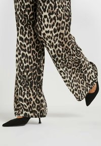 Pantaloni a gamba larga in stampa leopardo, in tessuto nero e beige, caratterizzati da una textura liscia e un design morbido, abbinati a tacchi a punta neri.
