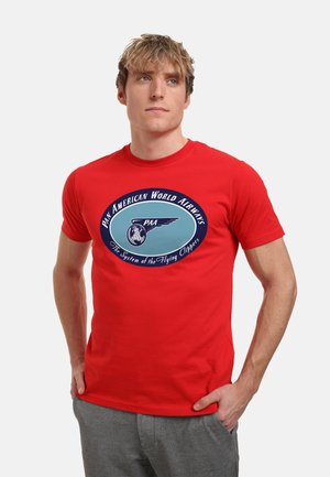 Rød bomulds t-shirt med et cirkulært grafik, der viser "Pan American World Airways," et blåt flydesign og tekst nedenunder. Kortærmet, rund hals.