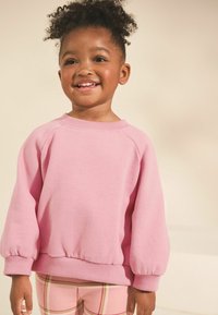 Sweatshirt rose avec un col rond et des manches bouffantes. Texture de tissu douce et poignets côtelés. Porté avec des leggings à carreaux.