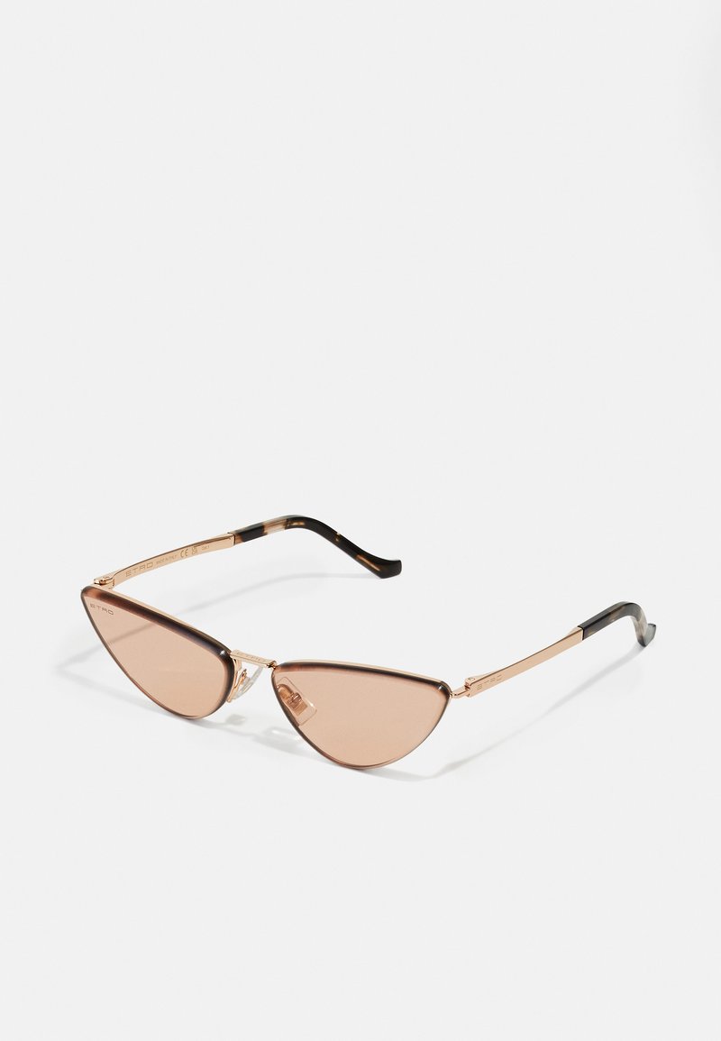 Γυαλιά ηλίου cat-eye με καφέ φακούς, χρυσό μεταλλικό σκελετό και μαύρες λεπτομέρειες στους βραχίονες. Κομψός σχεδιασμός με γωνιώδη σχήματα.