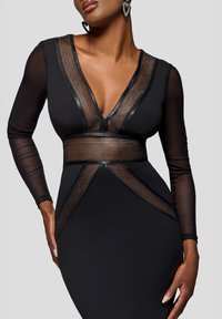 Zwarte lange-mouwen jurk met een diepe V-hals, doorschijnende inzetstukken en gestreepte accenten aan de taille, die een aangesloten silhouet benadrukken.