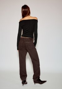 Czarny top z długim rękawem i odkrytymi ramionami, zestawiony z brązowymi spodniami w wzór geparda, ozdobionymi dekoracyjnymi metalowymi elementami.