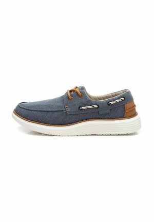 Zapato de lona azul marino con una suela blanca, acentos marrones y cordones decorativos; cuenta con una punta redondeada y un interior acolchado.