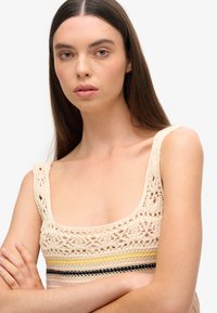 Haken top met een vierkante halslijn, met een beige basis, kleurrijke gestreepte accenten (geel, roze, zwart) en open kantdetails.