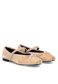 Bailarinas de terciopelo en beige con suela de goma, que cuentan con una tira cruzada adornada con tachuelas de plata y un lazo en la parte delantera.