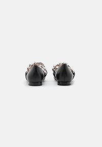 Paire de chaussures plates en cuir noir avec des détails en chaîne argentée, vue de dos, sur fond blanc.