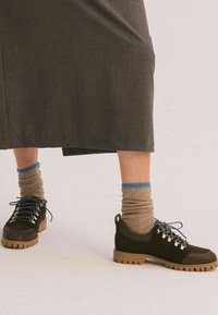 Scarpe in suede nere con lacci blu e suole in gomma grigia, abbinate a calze leggermente marroni con texture e un accent blu.
