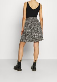 Zwarte geribbelde tanktop gecombineerd met een uitlopende rok met bloemenpatroon in zwart en wit. Het model draagt zwarte enkellaarzen met gele accenten.