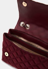 Bordowy pikowany portfel z złotym zapięciem na zatrzask, otwarty aby pokazać dwa wewnętrzne przegródki i beżową podszewkę.