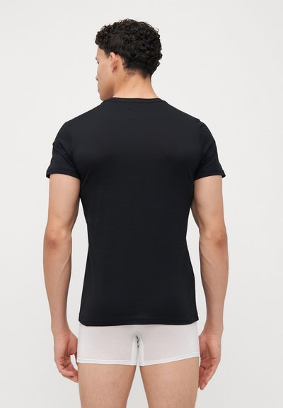 Μαύρο κοντομάνικο μπλουζάκι από λείο, ελαφρύ ύφασμα. Εφαρμοστό σχέδιο, στρογγυλή λαιμόκοψη και ελάχιστες λεπτομέρειες. Φορεμένο με λευκά σλιπ.