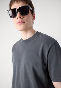 Szürke pamut póló laza szabással és kerek nyakkivágással. Fekete, oversized napszemüveg szögletes kerettel és diszkrét fém részletekkel.