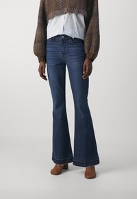 Jeans a zampa d'elefante in denim blu scuro, con vita media, classico design a cinque tasche e orlo grezzo. Abbinati a un maglione in tessuto strutturato.