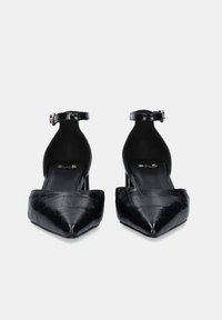 Zapatos de tacón negro con puntera afilada, hechos de cuero acolchado; cuentan con una correa en el tobillo con hebilla y un tacón estrecho y transparente.