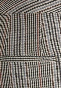 Teksturowana tkanina prezentująca naprzemienne czarne, białe i czerwone paski pod różnymi kątami, z detalem kieszeni z przodu.