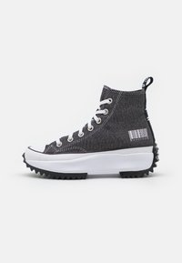 Höga sneakers gjorda av svart tyg med vita snörningar, en vit mellansula och en robust svart yttersula. Har en streckkoddesign på sidan.