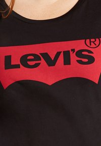 Tricou negru cu un mare logo roșu în formă de aripă de liliac, cu "Levi's" scris cu litere mari negre. Material moale din bumbac, guler rotund, mâneci scurte.