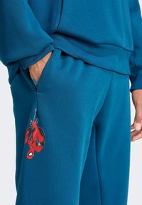 Blue sweatshirt and matching sweatpants feature a red Spider-Man graphic. Fabric appears soft with a smooth texture, and there are side pockets.