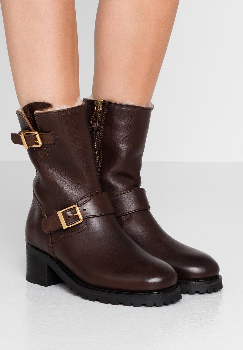 Hnědé kožené kotníkové boty s texturovaným povrchem, s jazýčky zlaté barvy a bočním zipem. Patkový podpatek a polstrovaný límec pro pohodlí.