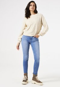 Lichtbeige gestructureerde trui met lange mouwen, gecombineerd met mid-blue skinny jeans en bruine veterlaarzen met dikke witte zolen.