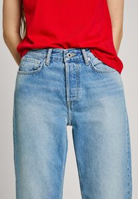 Gai zila denima bikses ar augstu vidukli, taisnām kājām un piecu kabatu dizainu. Iespējama priekšējā poga un smalks nodilums.