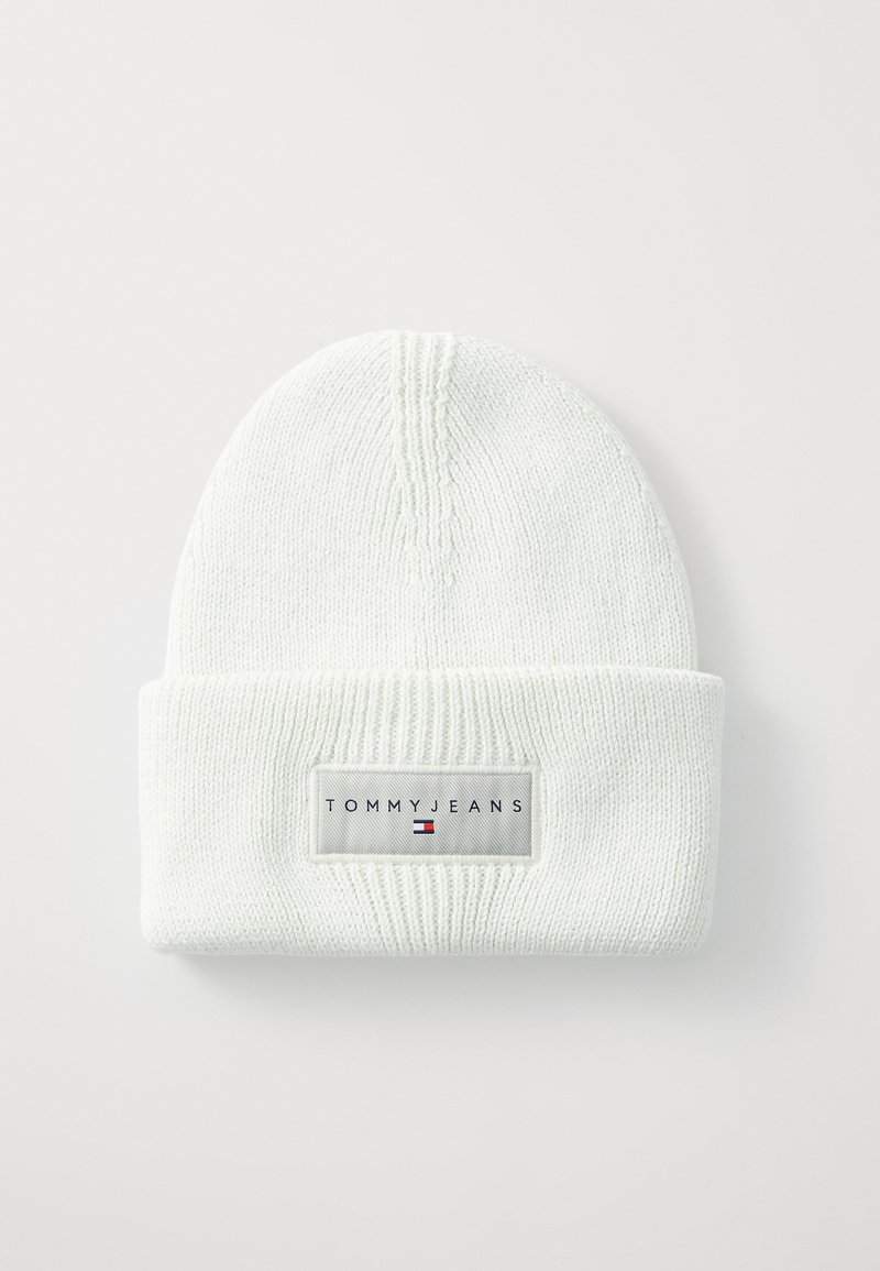 Bonnet en tricot blanc avec texture côtelée, doté d'un revers et d'une étiquette rectangulaire portant l'inscription "TOMMY JEANS" avec un logo bleu et rouge.