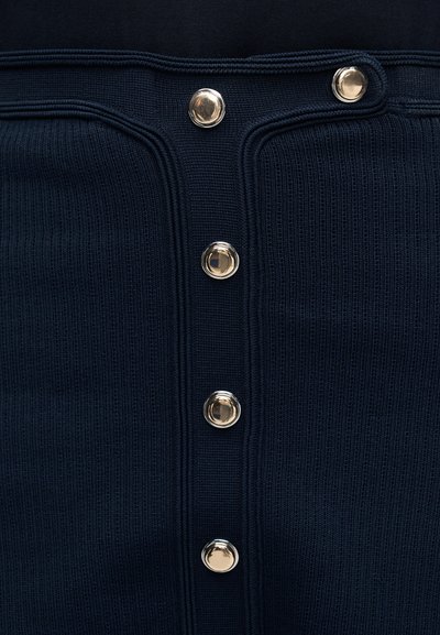 Κοντινό πλάνο από ύφασμα σε σκούρο μπλε με ριγωτή υφή και πέντε λάμπουν στρογγυλά ασημένια κουμπιά τοποθετημένα κατά μήκος κατακόρυφα.