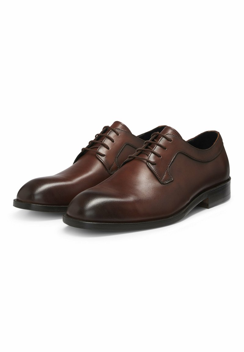 Chaussures de ville en cuir marron avec des orteils ronds, un laçage, une texture lisse et des accents de couture subtils le long des côtés.