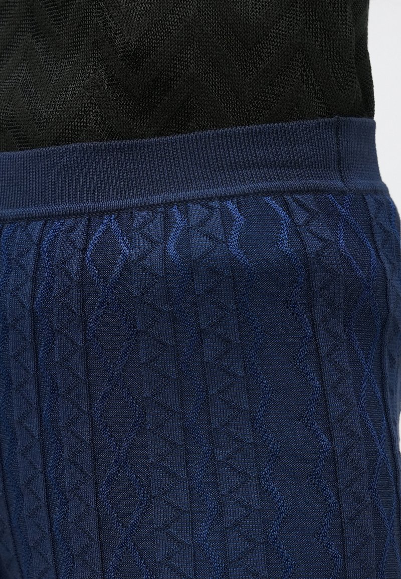 Pantaloni blu scuro lavorati a maglia con un motivo geometrico texturizzato. Presentano una cintura a costine e una superficie del tessuto liscia.